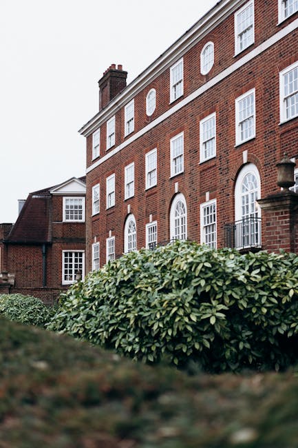 The image displays the facade of a stately Georgian townhouse, featuring a cream-colored exterior with classical architectural elements such as tall, fluted columns supporting a balcony with a balustr
